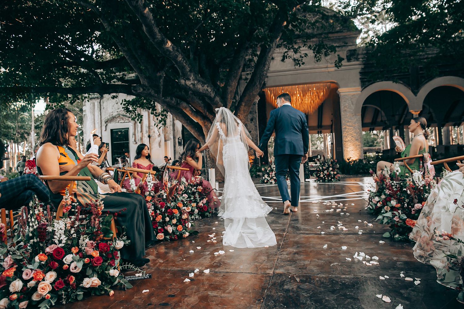 A wedding ceremony outdoors with floral decorations and white petals scattered on the ground.
