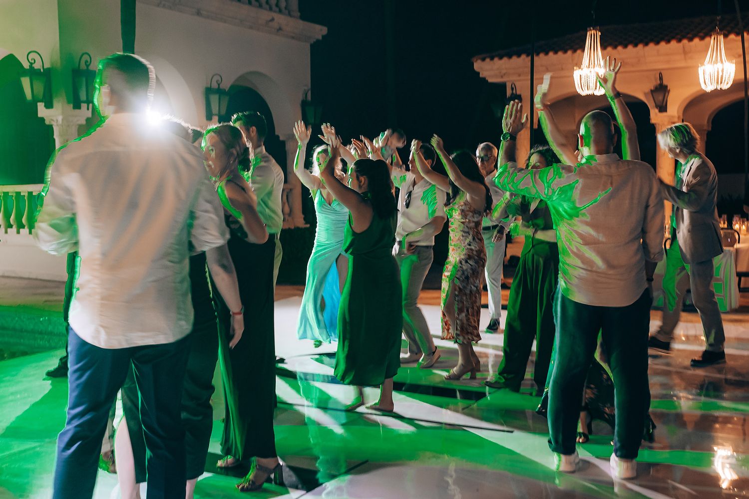 People dancing together at a social event with green lighting effects illuminating the dance floor.