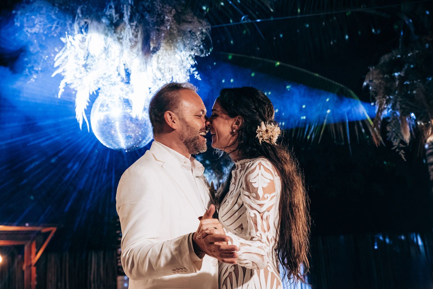 A couple shares a romantic dance moment under dramatic blue lighting at an outdoor evening celebration.
