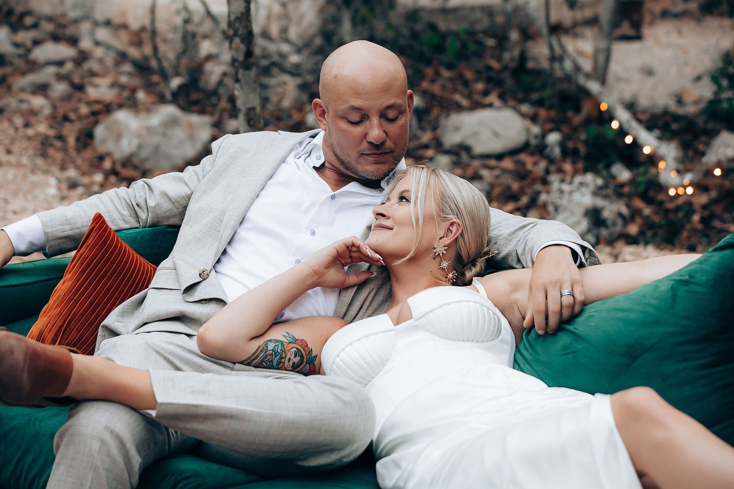 A couple relaxes together on green velvet furniture in casual wedding attire.