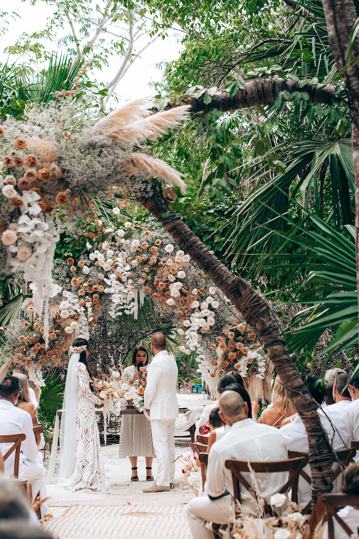 Outdoor garden wedding ceremony with pampas grass decorations and guests seated in white chairs.