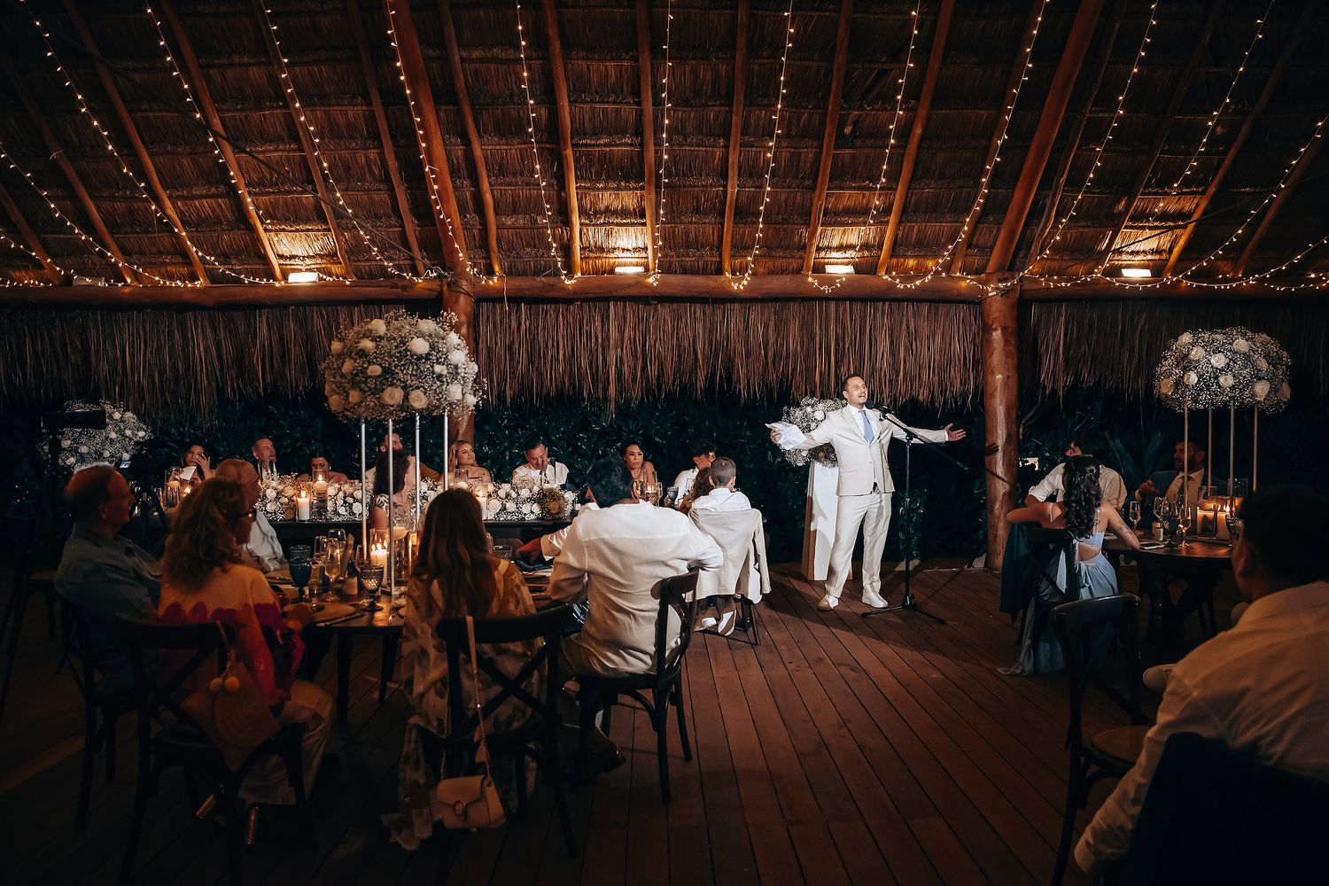 Wedding reception venue with warm string lights creating an intimate atmosphere under a thatched roof.