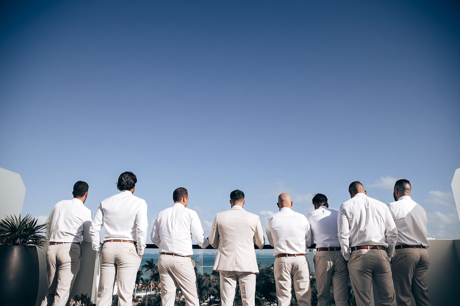 A group of people in white shirts stand together in a line against a blue sky background.