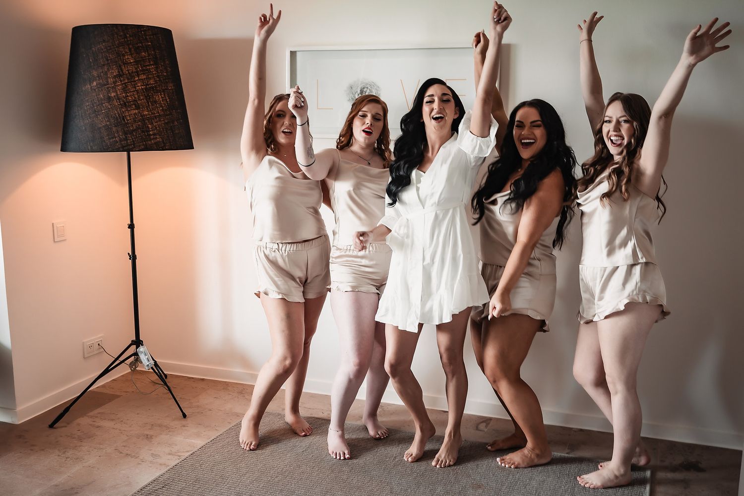 A group in white dresses jumps and dances together in a bright indoor space with brick walls.