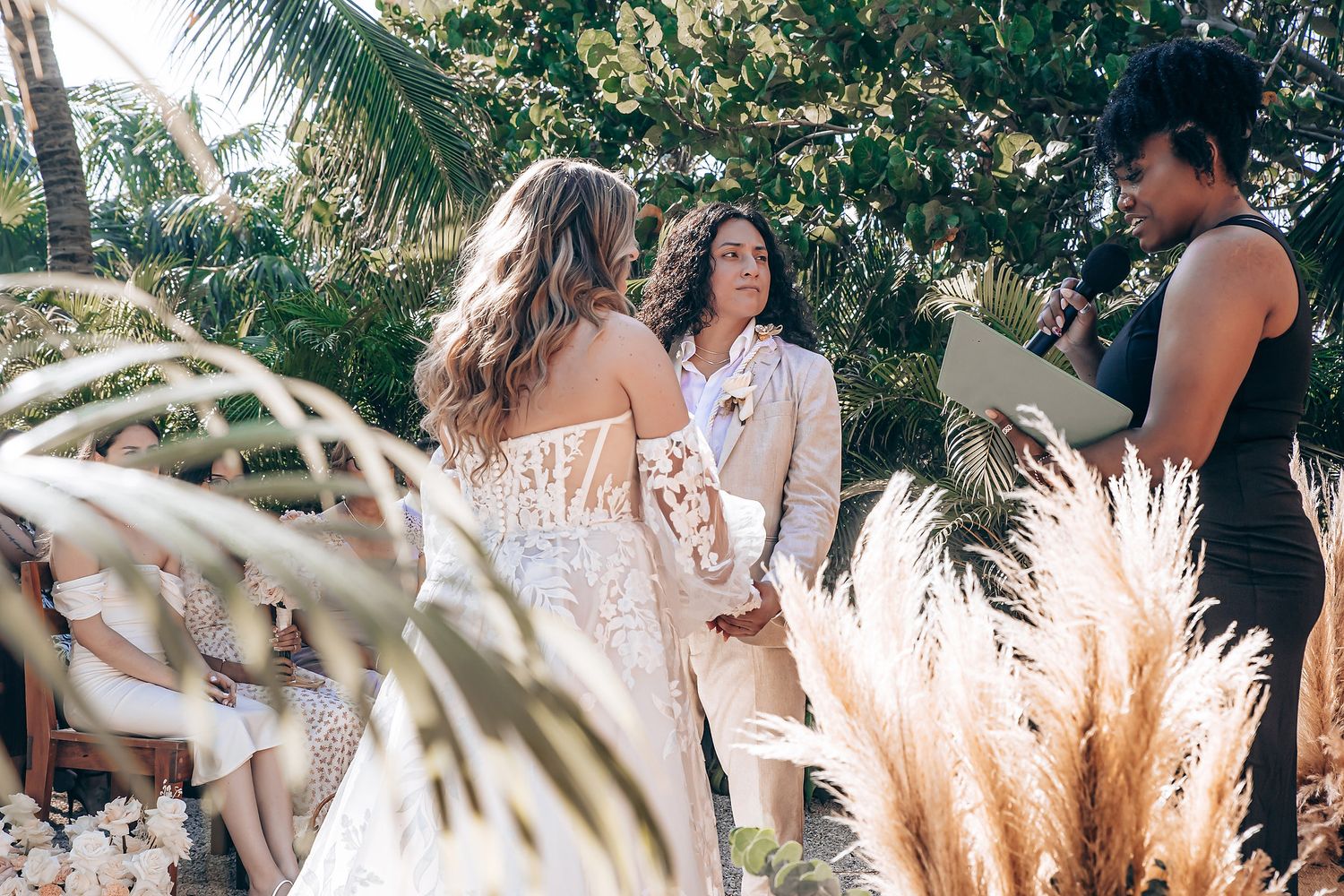 A tropical outdoor ceremony with pampas grass decorations and palm trees in the background.