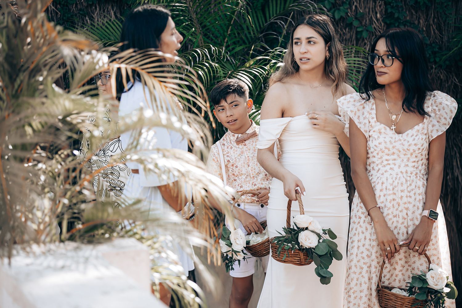 A group of people in light-colored dresses and formal attire gather outdoors for a wedding celebration.