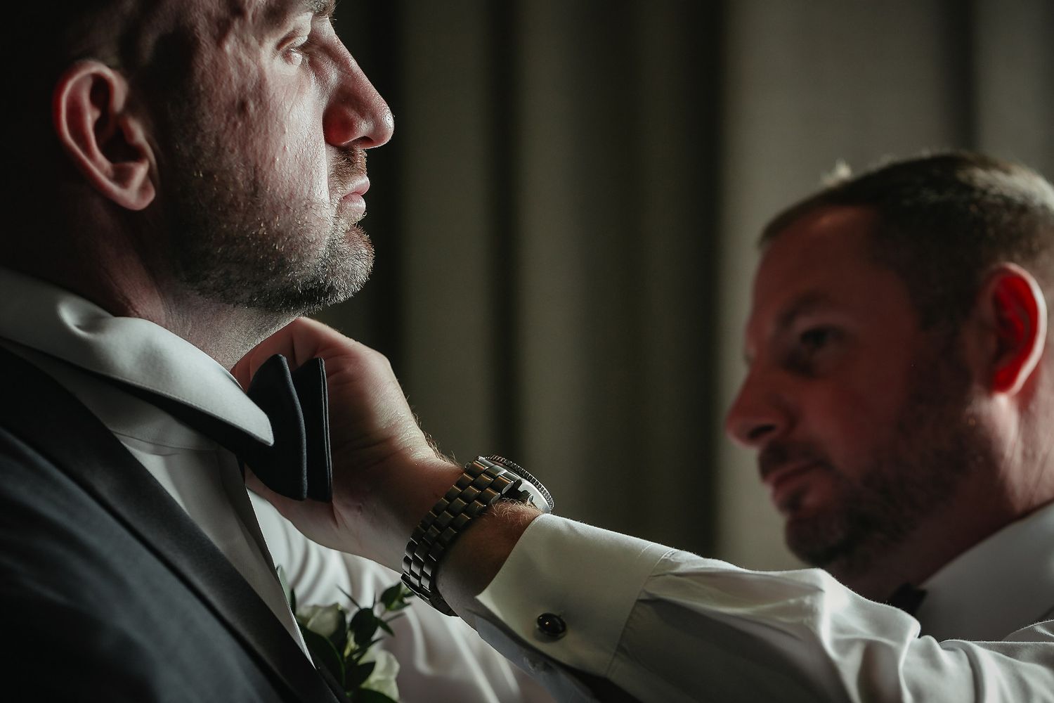 Man in formal attire adjusts his tie while getting ready in dramatic lighting.