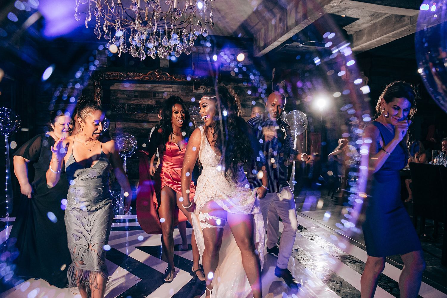 Nightclub party scene with dancing crowd under purple lighting and disco ball atmosphere.