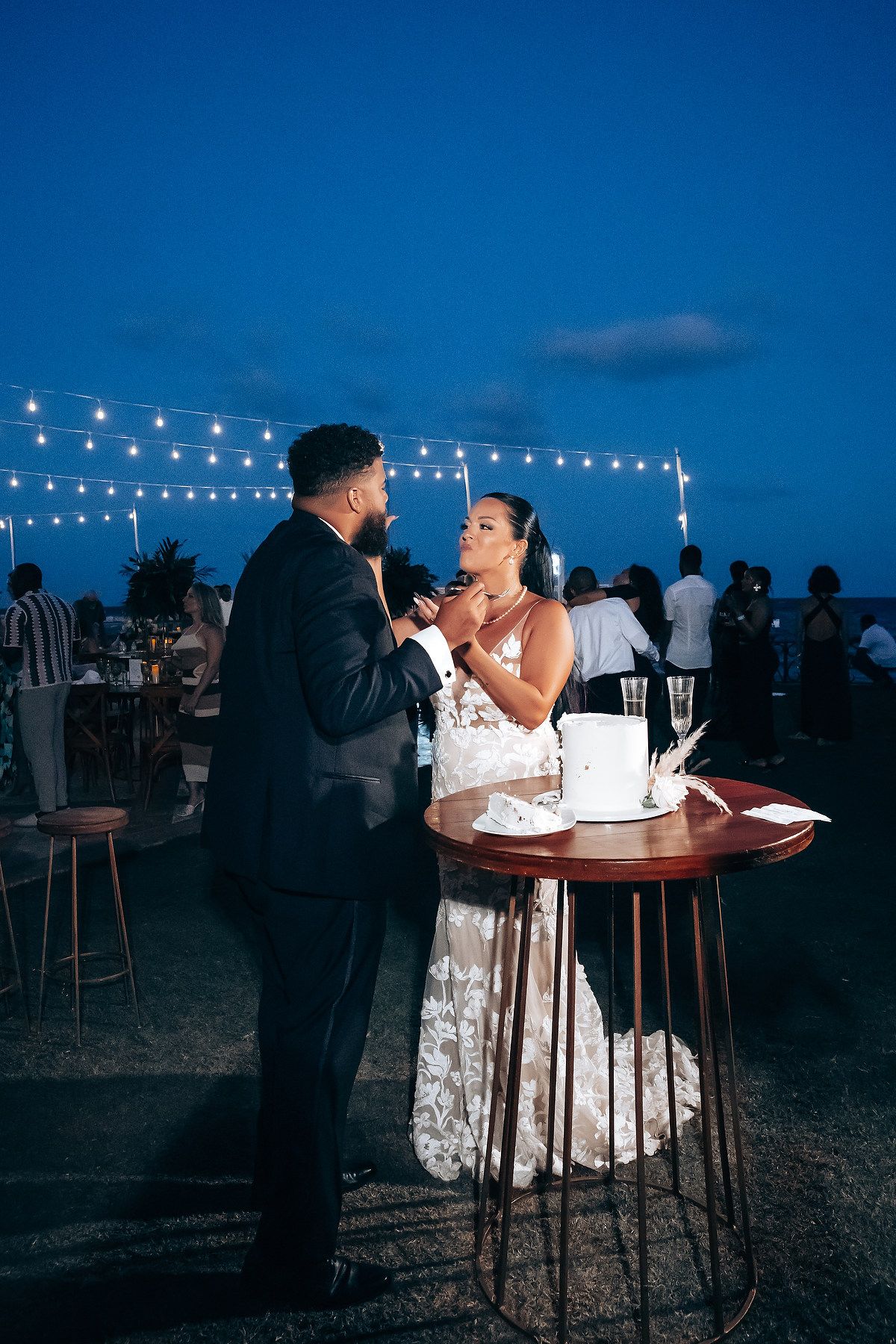 Nighttime wedding reception with string lights and couple enjoying intimate moment at cocktail table.