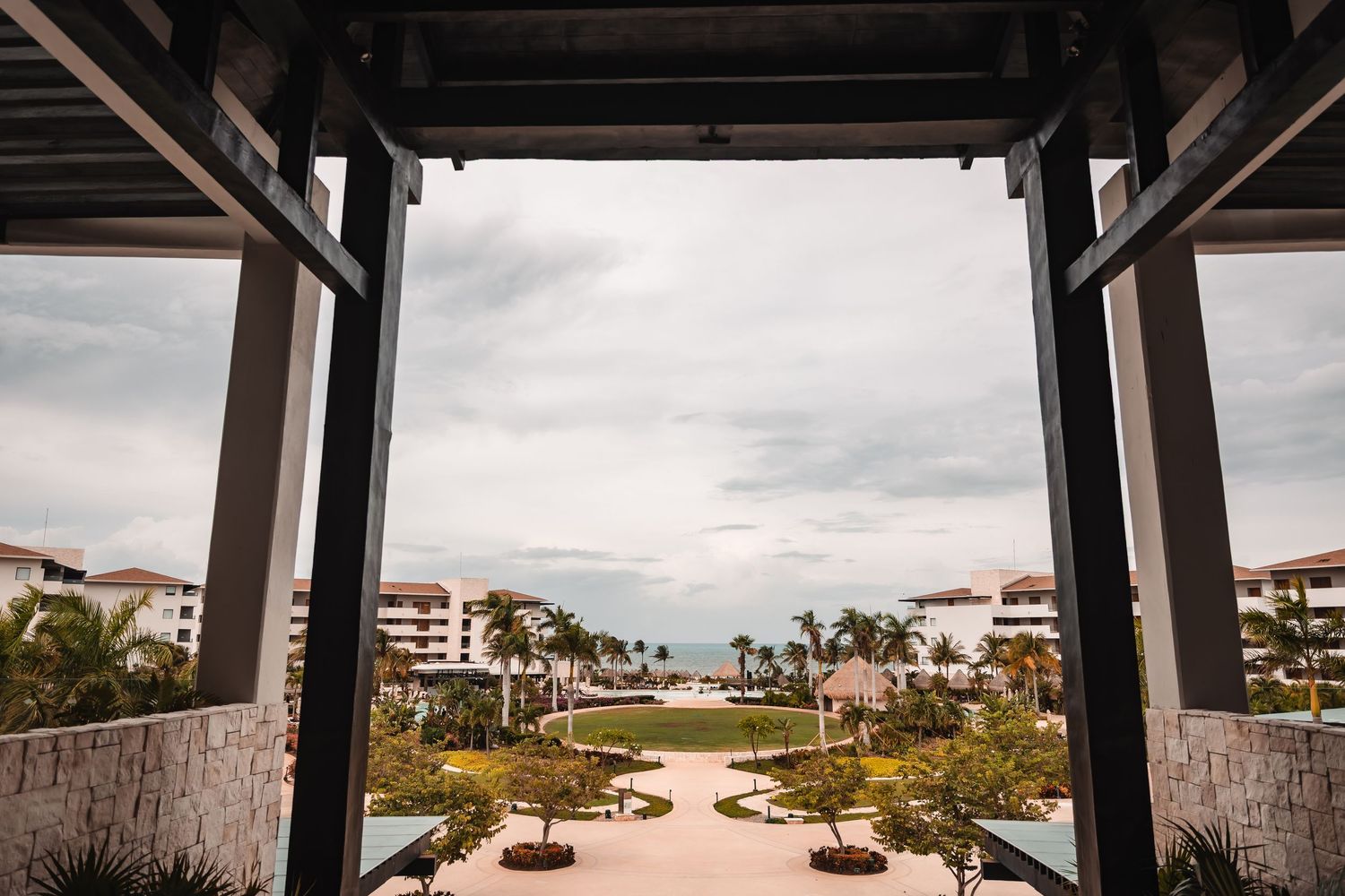 Covered beachfront walkway with palm trees and resort buildings in the background.
