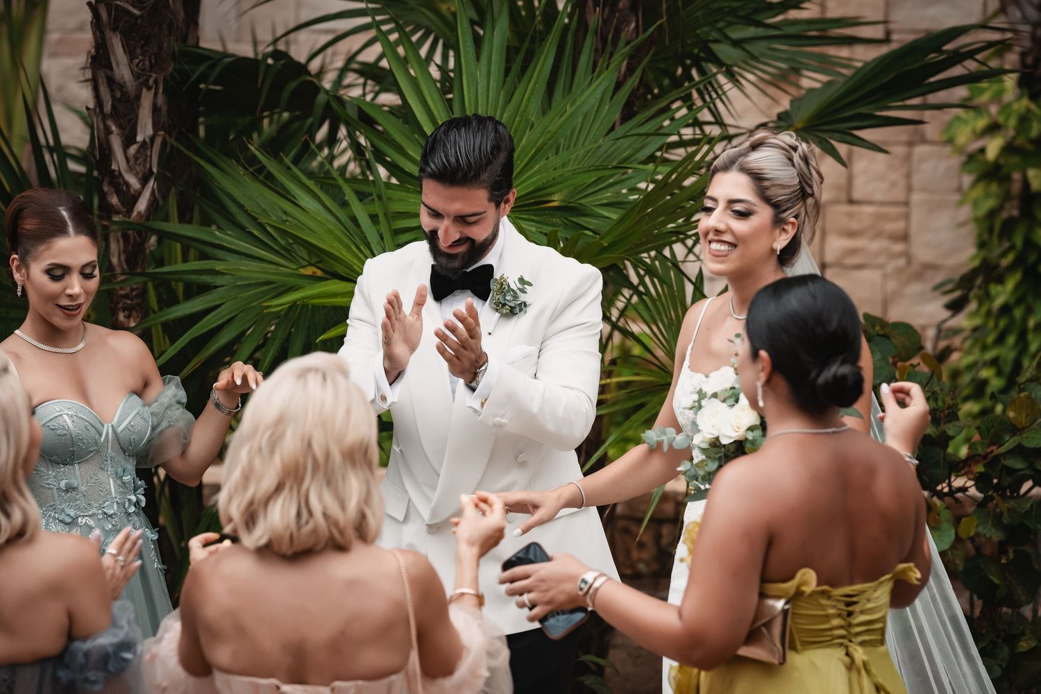Wedding party celebrates with bridesmaids in pastel dresses against palm trees.