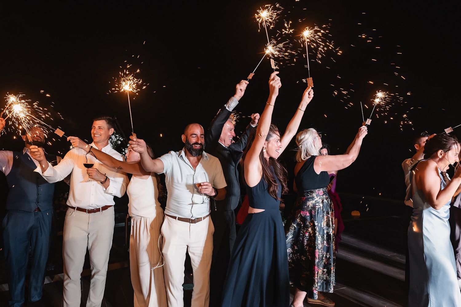 Celebration guests raise sparklers in unison during a festive outdoor nighttime event.