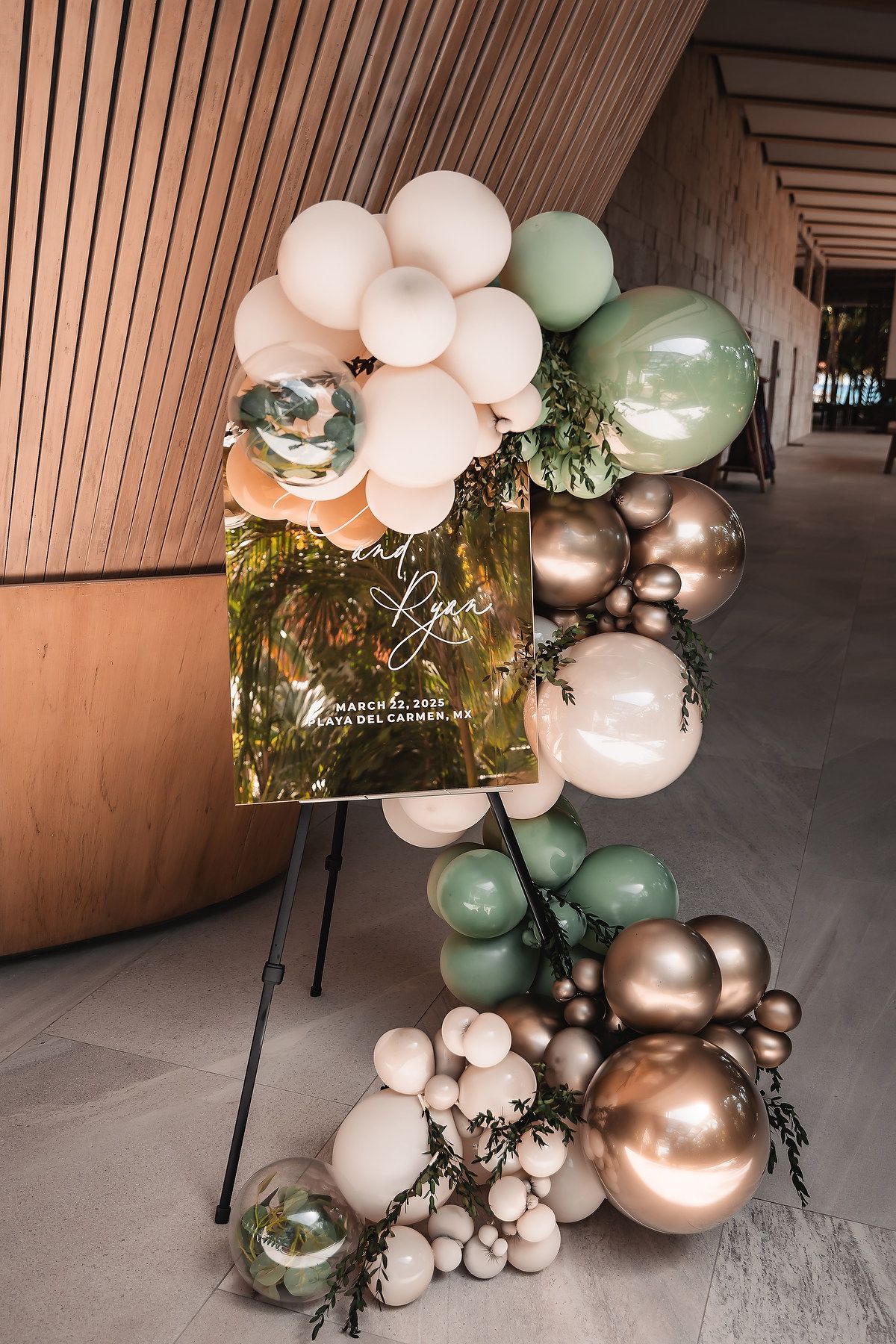 Elegant balloon arch installation with white, green, and gold balloons decorating an indoor venue space.