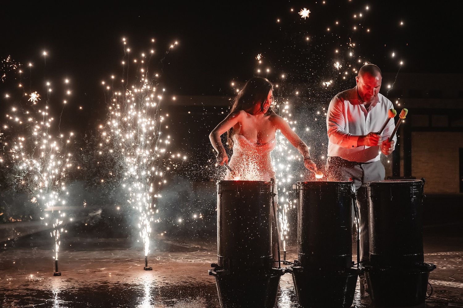 Couple igniting sparkling fireworks fountains at night during a romantic outdoor wedding celebration.