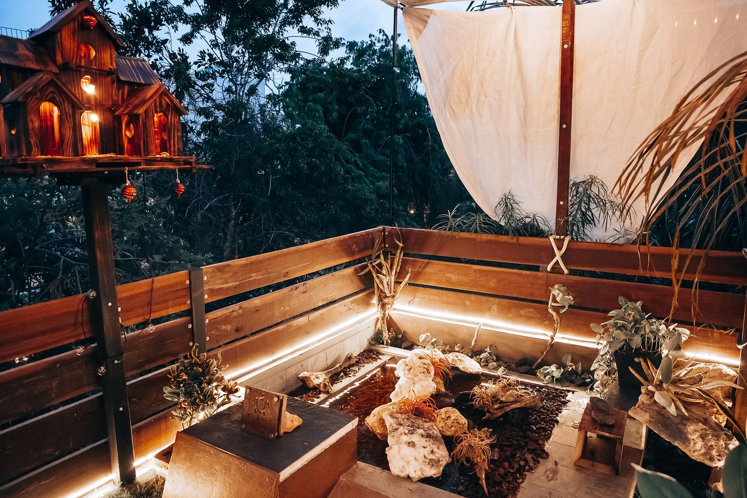 Cozy boho wedding lounge area with string lights, wooden decor, and draped fabric at dusk.