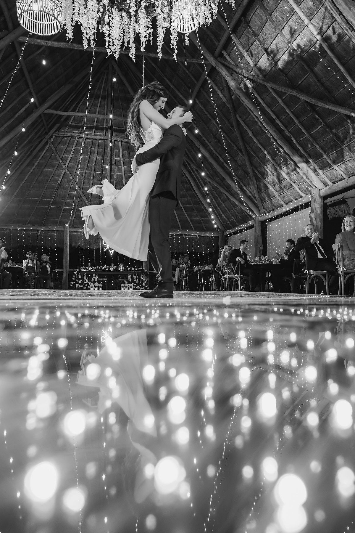 Black and white photo of a couple sharing their first dance at a wedding reception with bokeh lights on the dance floor.