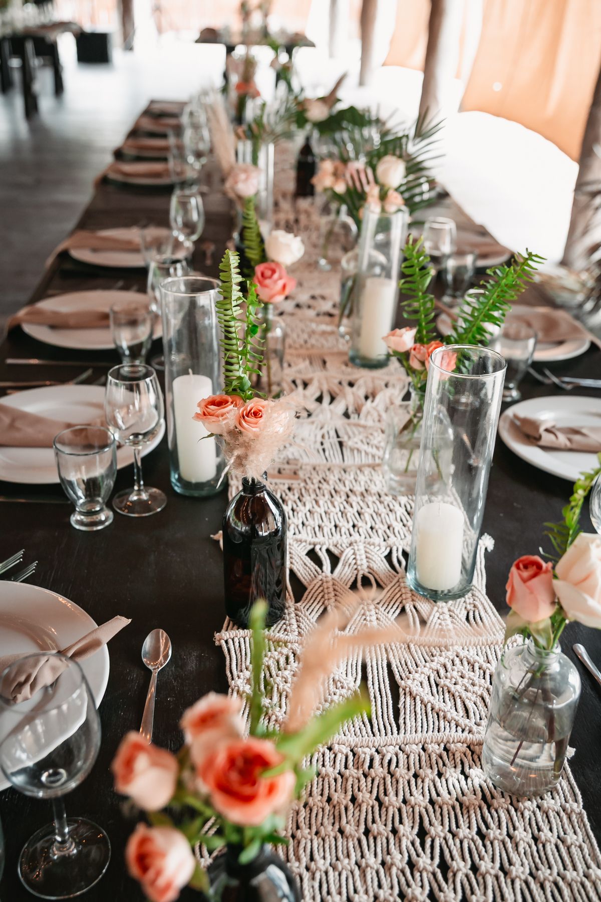 Elegant wedding reception table with macrame runner, candles, and pink roses centerpieces.