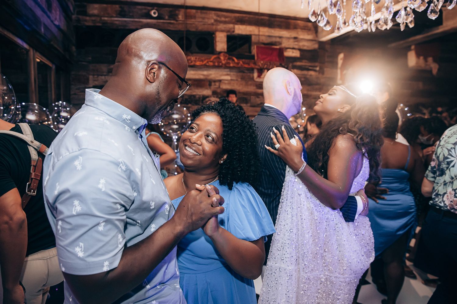 Guests dance together at a wedding reception in a rustic venue with ambient lighting.