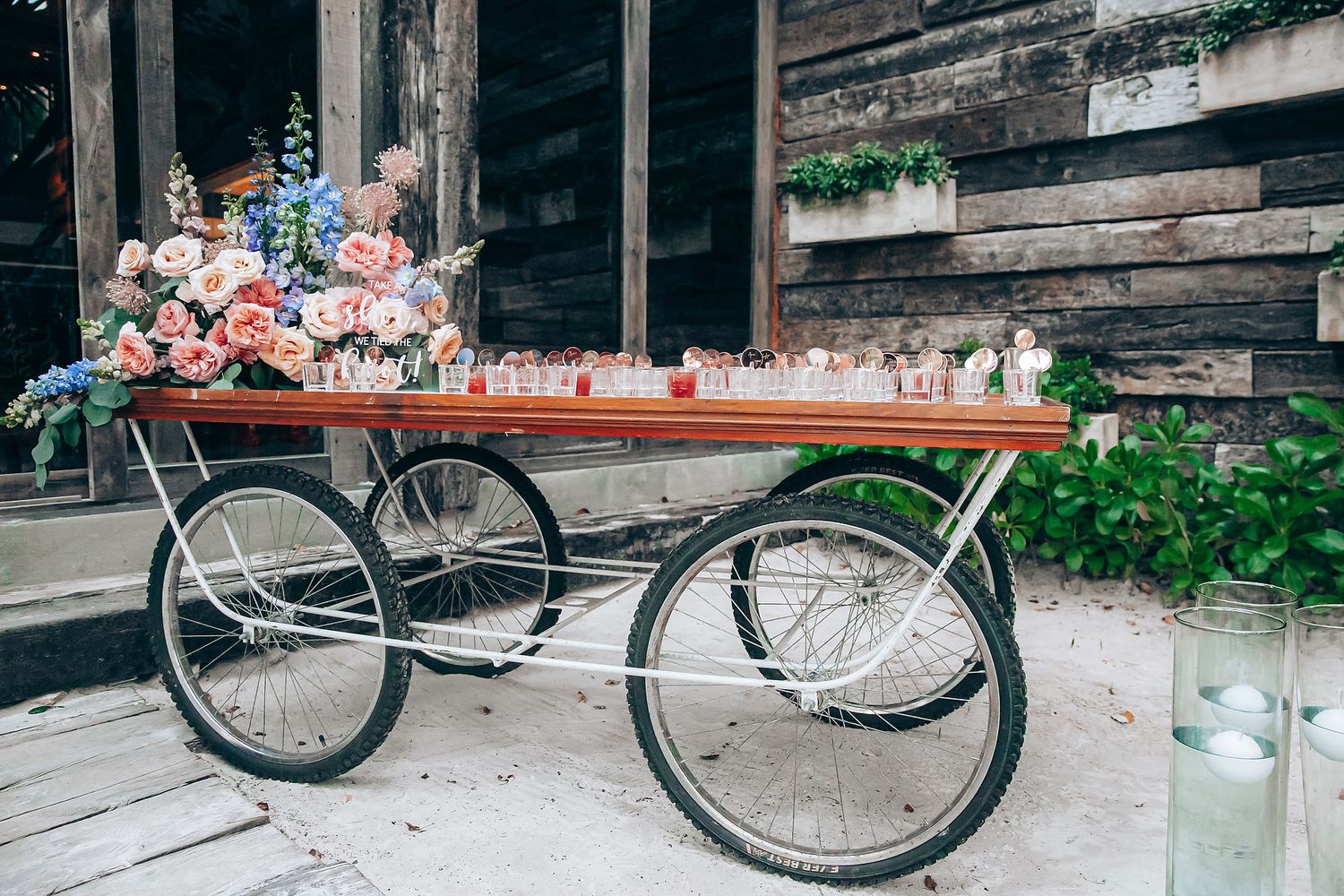 A vintage cart with wheels decorated with pink and white flowers against a rustic wooden wall.