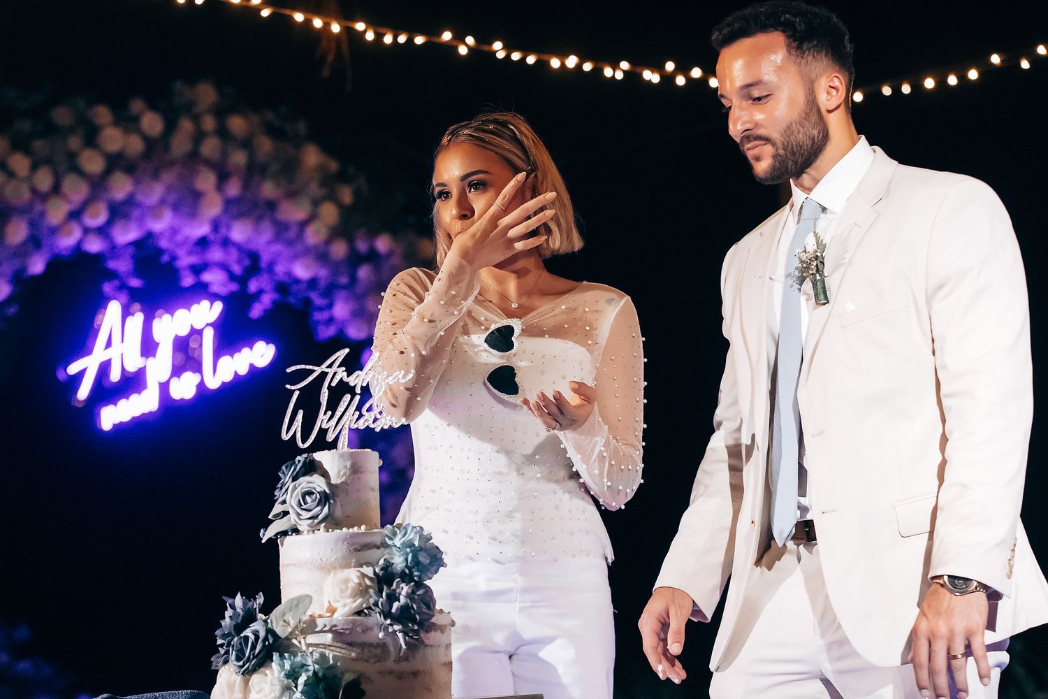 A couple shares an emotional moment while cutting their wedding cake under purple neon lighting.