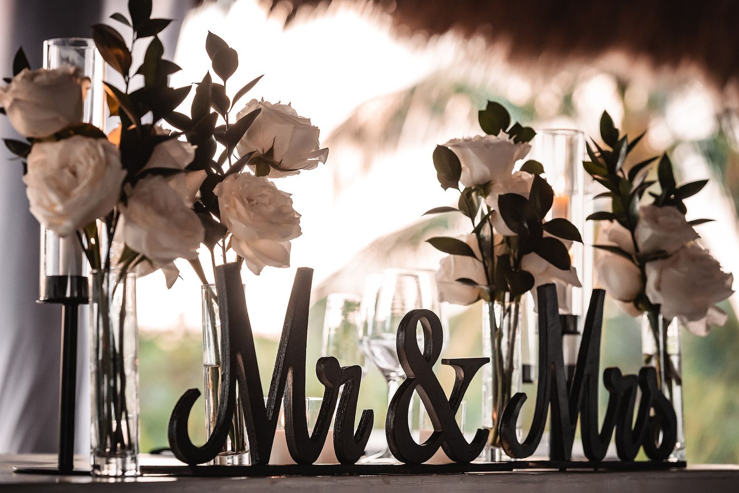 White floral arrangements and decorative 'Mr & Mrs' signage silhouetted against a bright background.