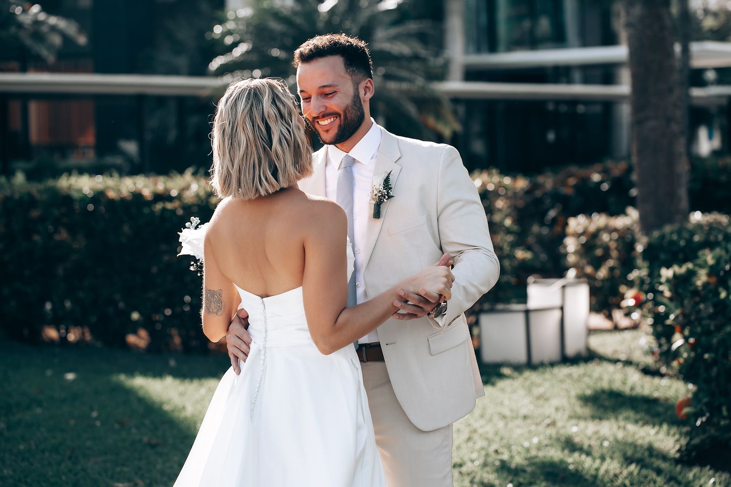 A joyful first look moment between a bride in white and groom in a light suit during an outdoor wedding celebration.