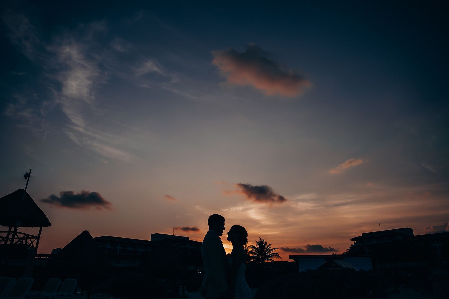 Dramatic silhouettes against a vibrant sunset sky during a beach wedding celebration.