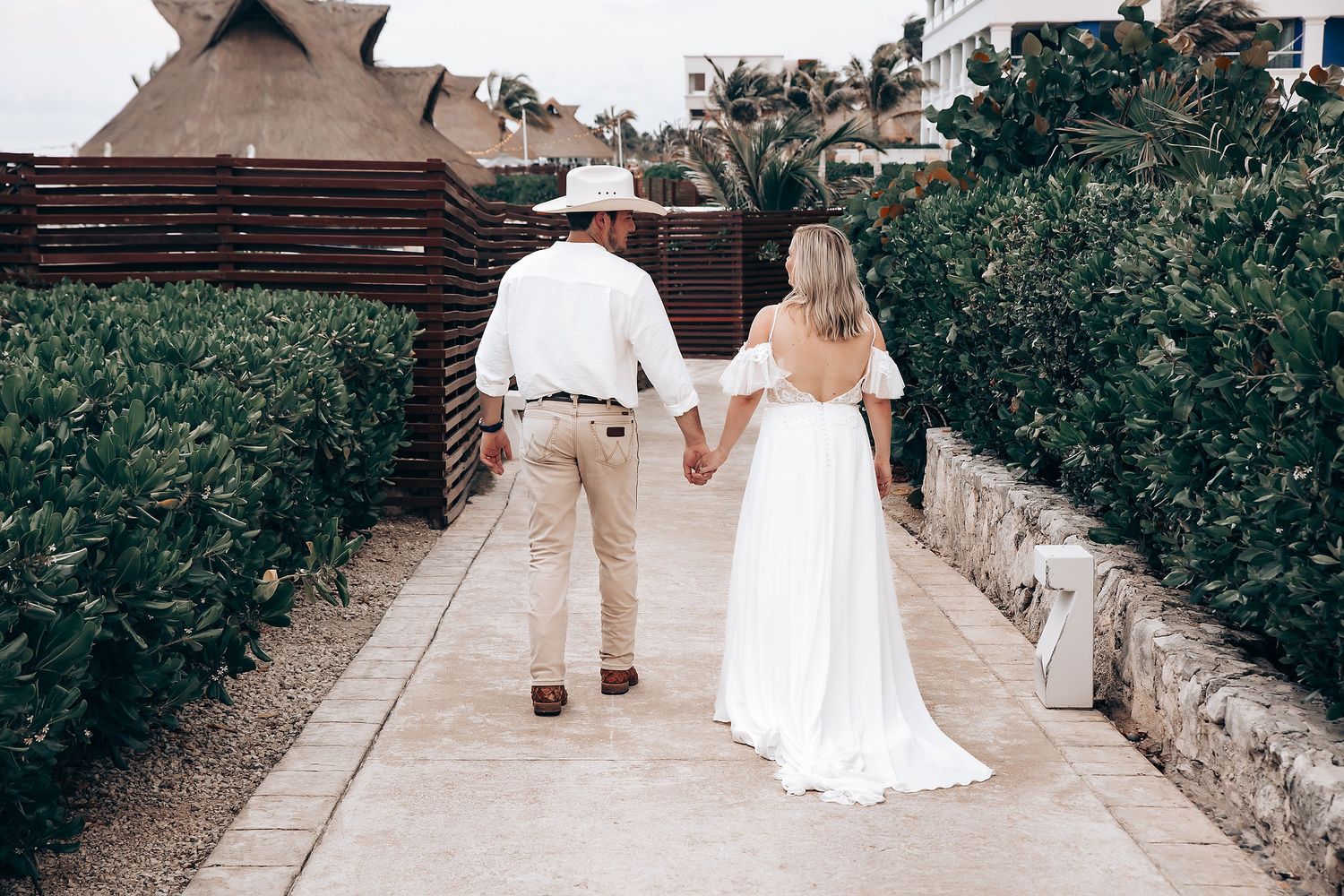 Couple walking down a garden path lined with greenery at an outdoor wedding ceremony.