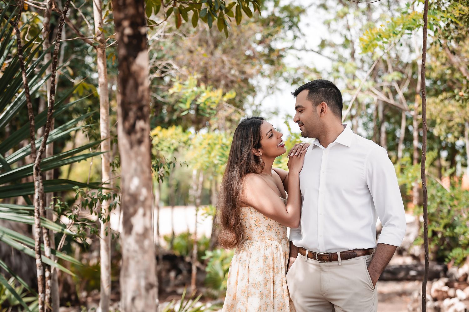 Romantic couple walks through sunlit garden pathway surrounded by tropical foliage.