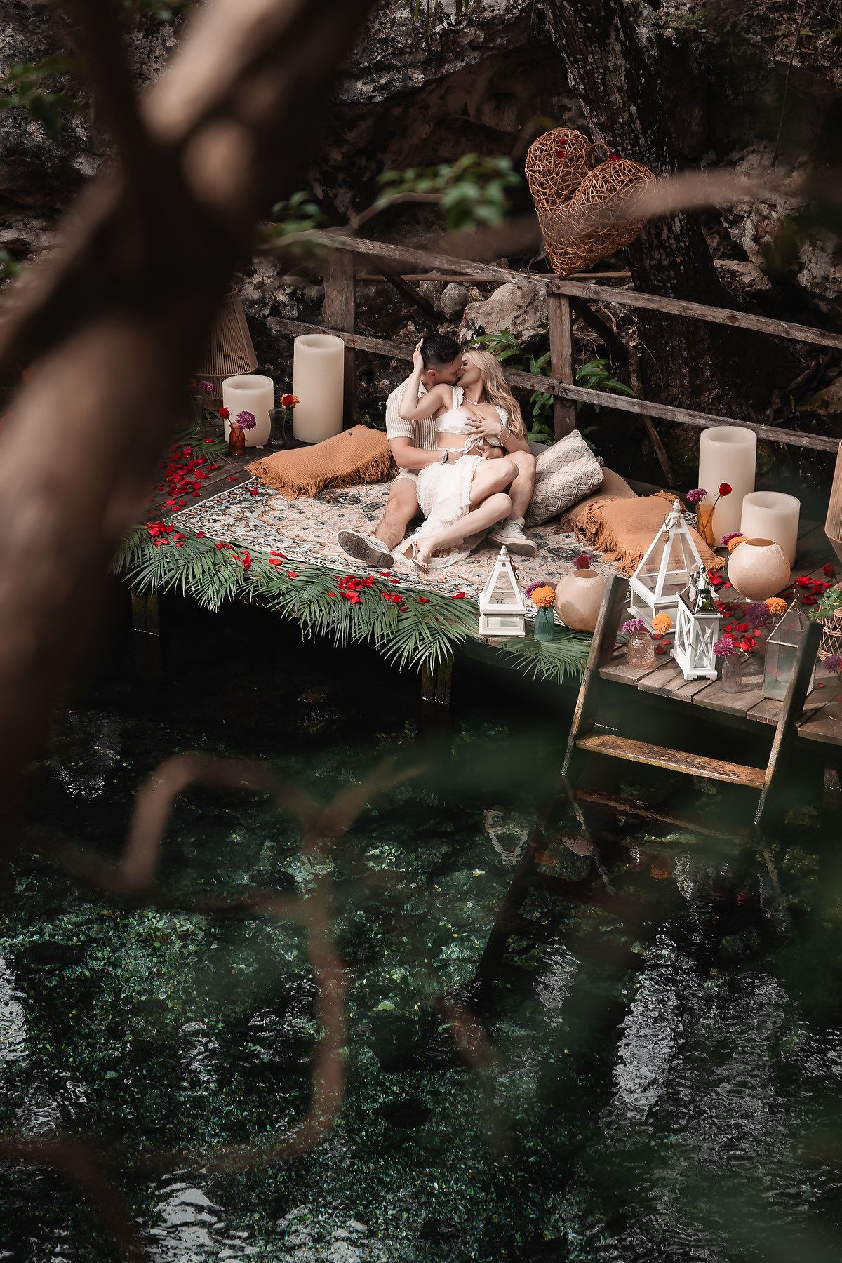 Romantic setup with lanterns and candles on wooden platform over dark water.