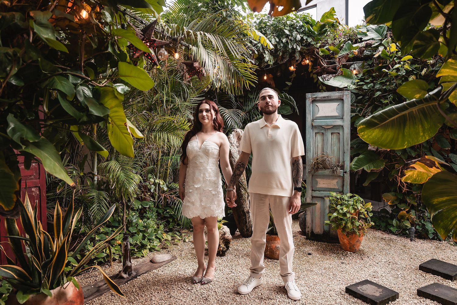 Couple walking through a tropical garden pathway lined with palm trees and vintage doors.