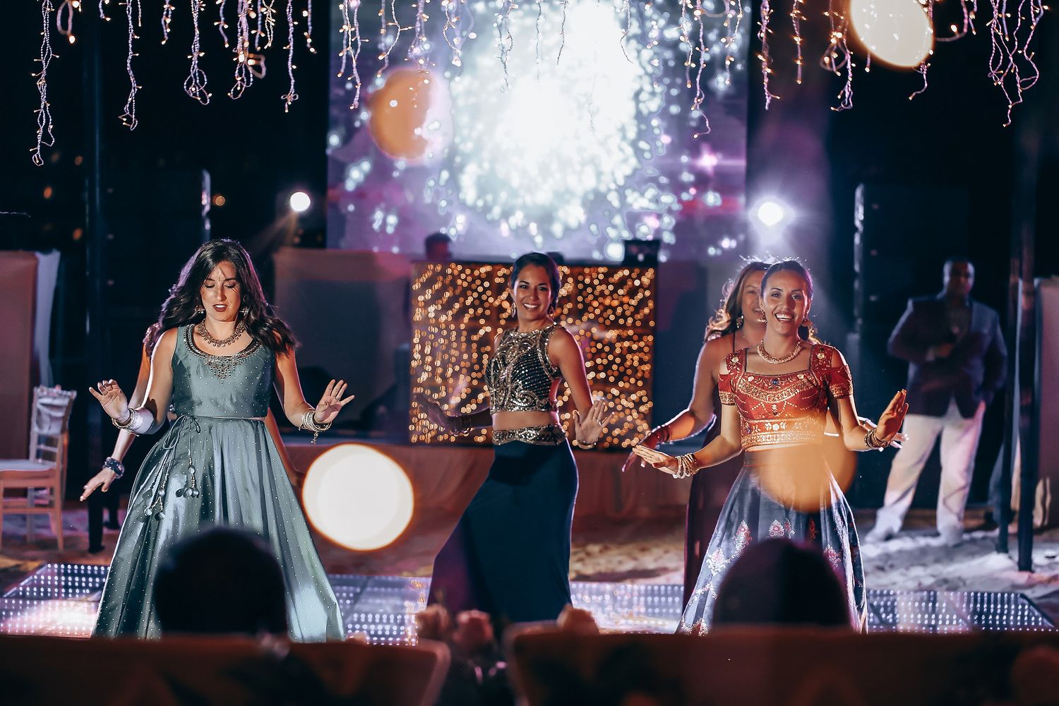 Three performers in elegant dresses sing on stage with dramatic lighting and decorative icicles hanging above.