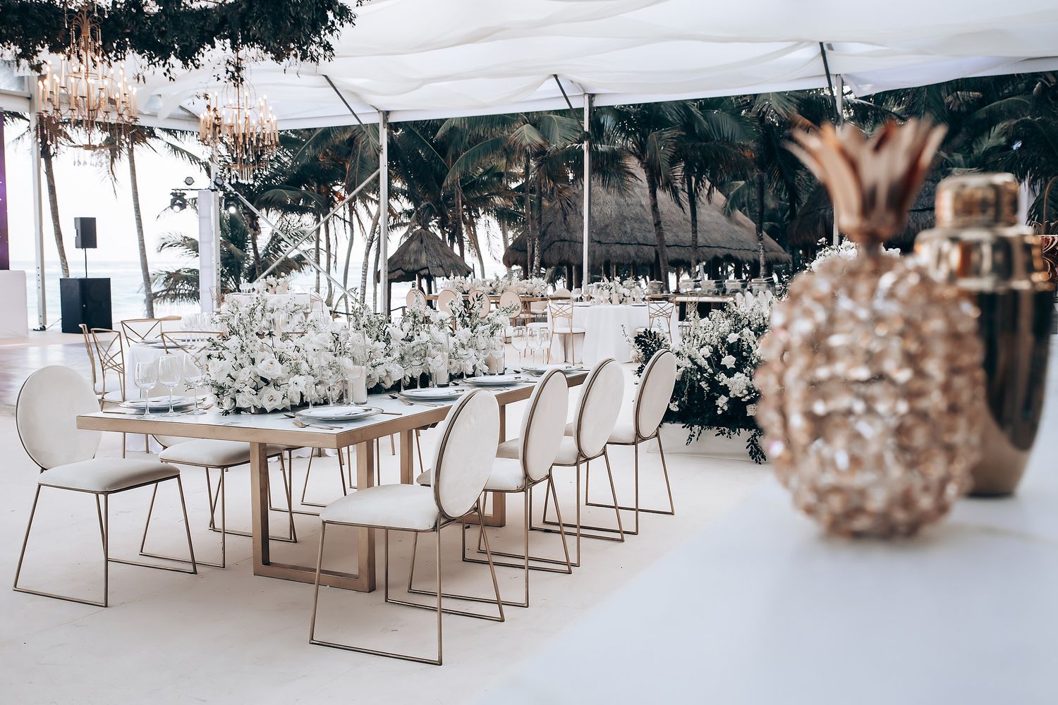 Modern white wedding reception setup with minimalist chairs and tropical decor elements.