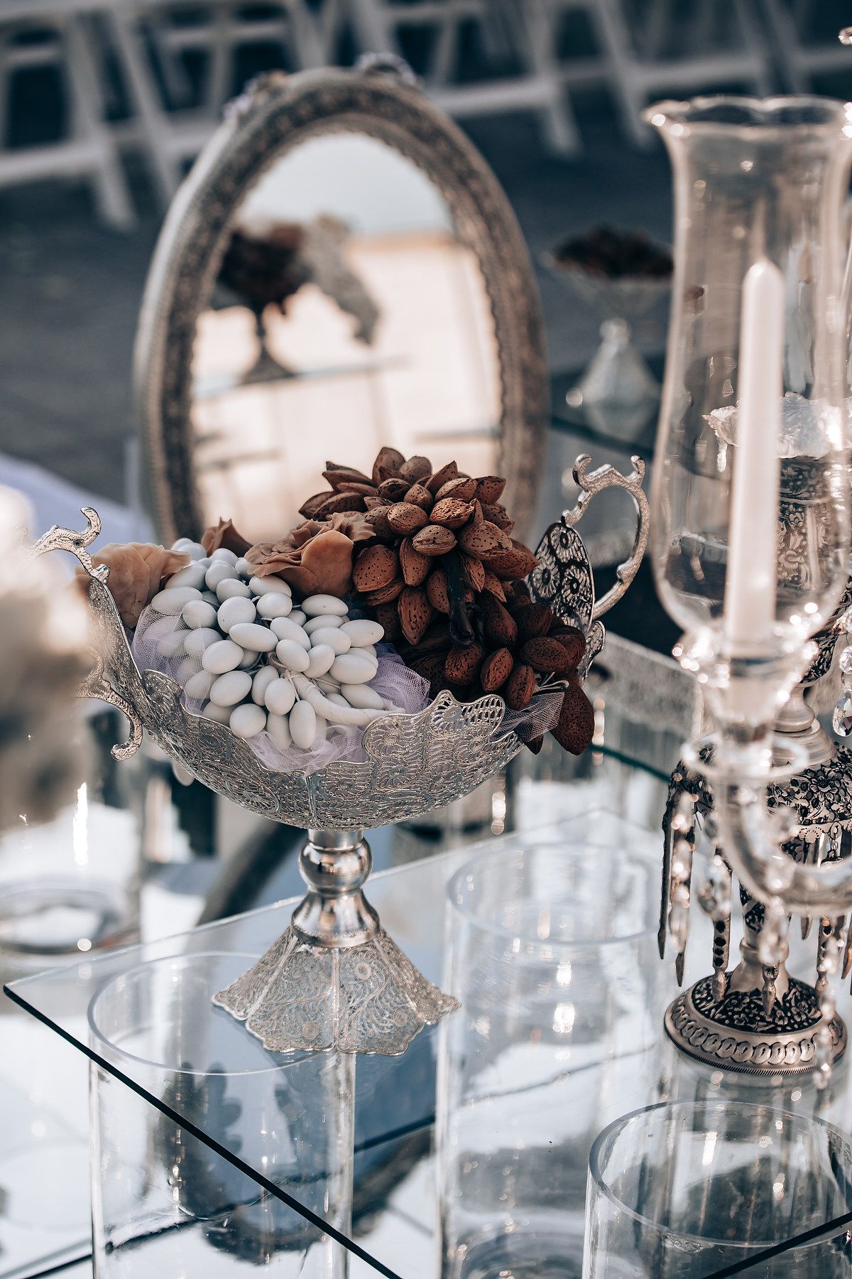Elegant silver bowls filled with decorative pinecones and white flowers on mirrored surfaces at a wedding reception.