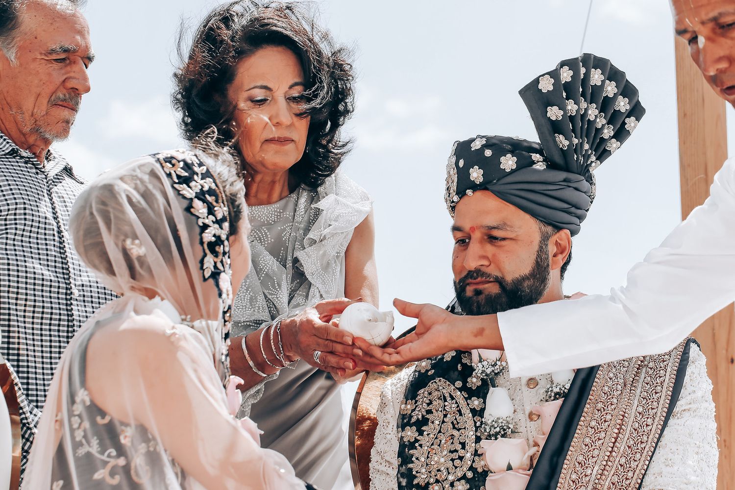 Wedding guests participate in a traditional ceremony ritual at an outdoor seaside venue.