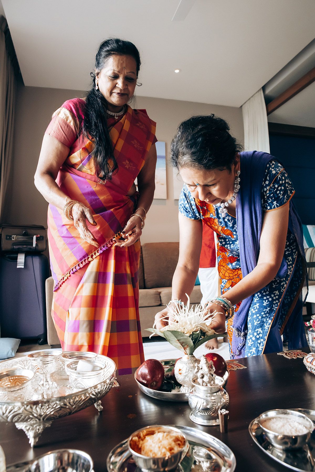 Two women prepare traditional food items and offerings in a modern kitchen setting.