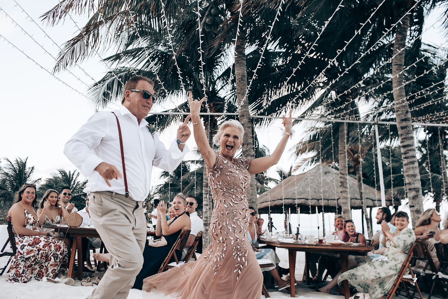Beachside celebration with people dancing and enjoying themselves under palm trees at a tropical resort.