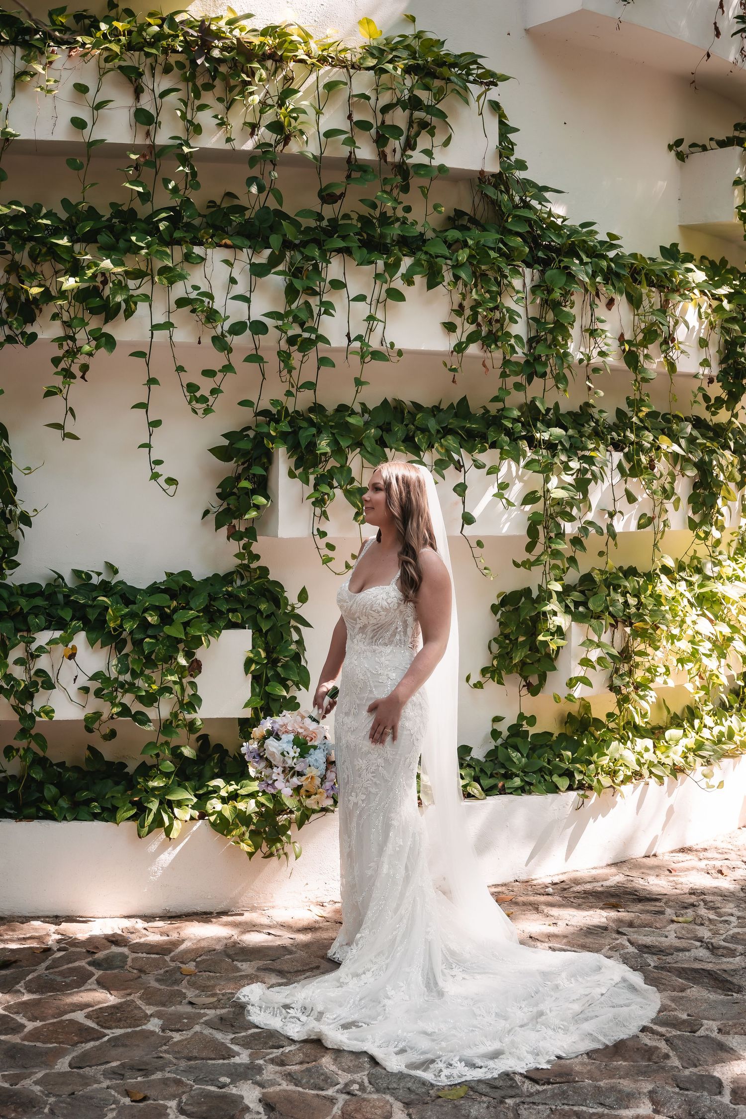 White lace wedding dress with flowing train against a stone patio with climbing vines.