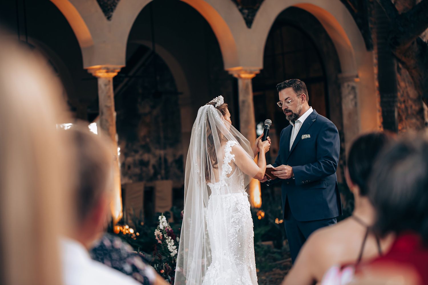 A couple exchanges vows during an intimate candlelit wedding ceremony in an elegant arched venue.