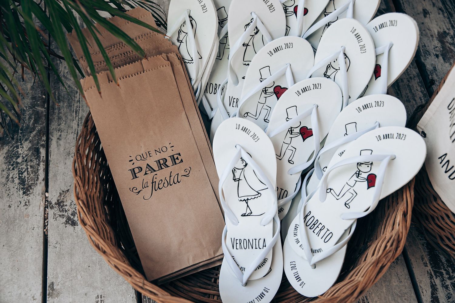 White flip flops with hand-drawn designs and a brown paper bag arranged in a wicker basket.