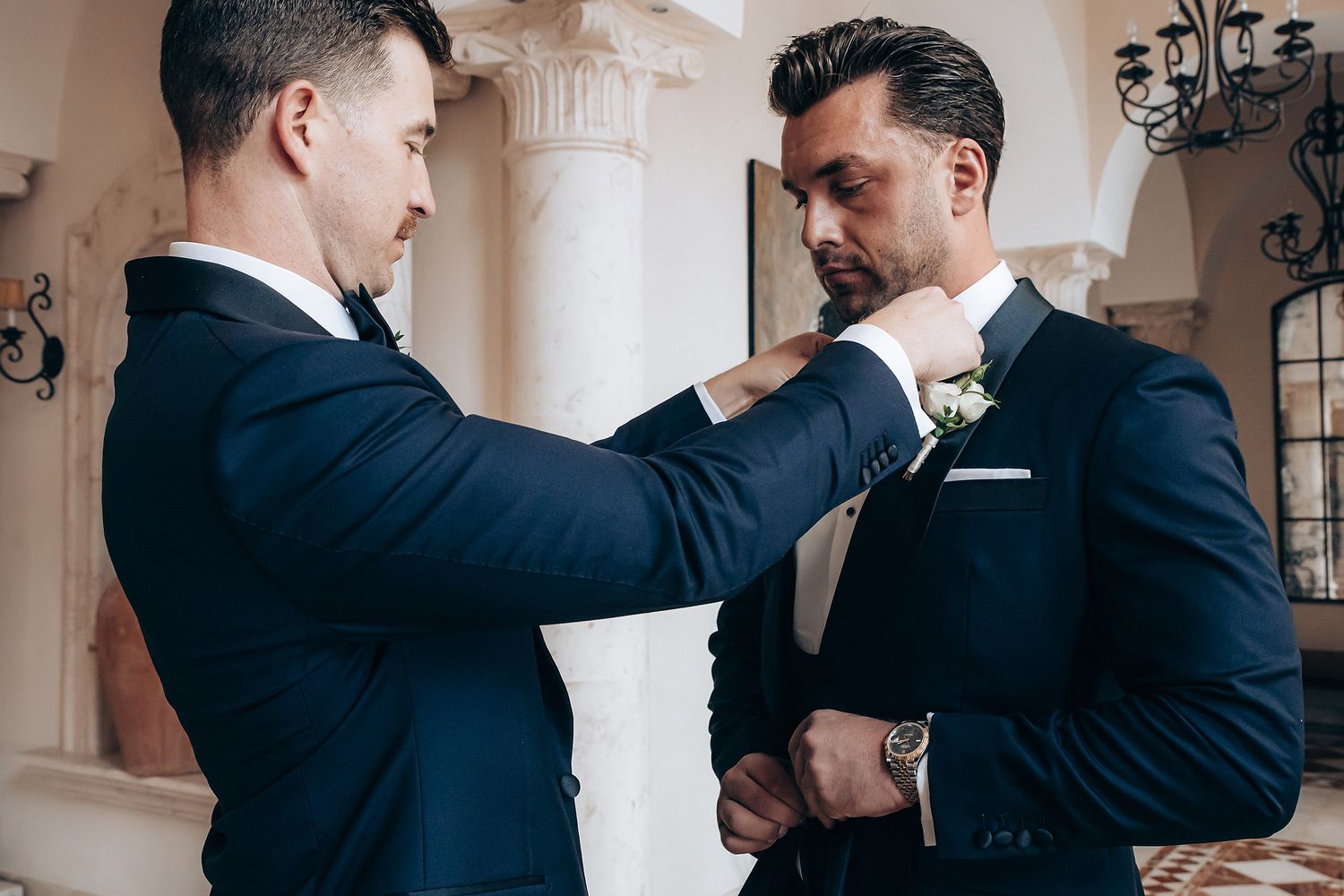 Groomsmen in dark suits help adjust each other's ties and boutonnieres before the ceremony.