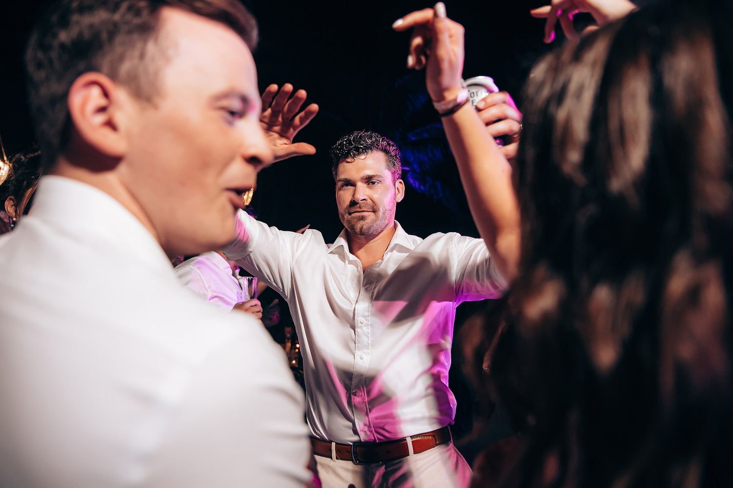 People dancing and celebrating at a lively party with pink lighting effects.
