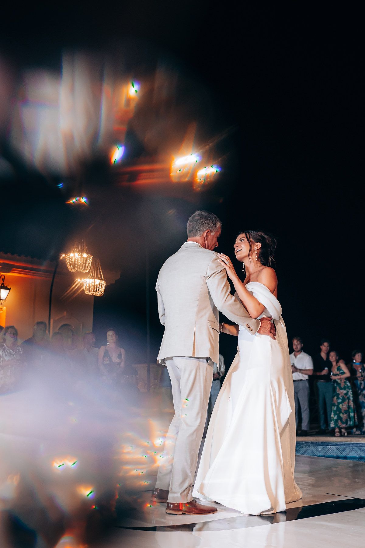 Couple shares their first dance in a misty ballroom under warm chandelier lighting.