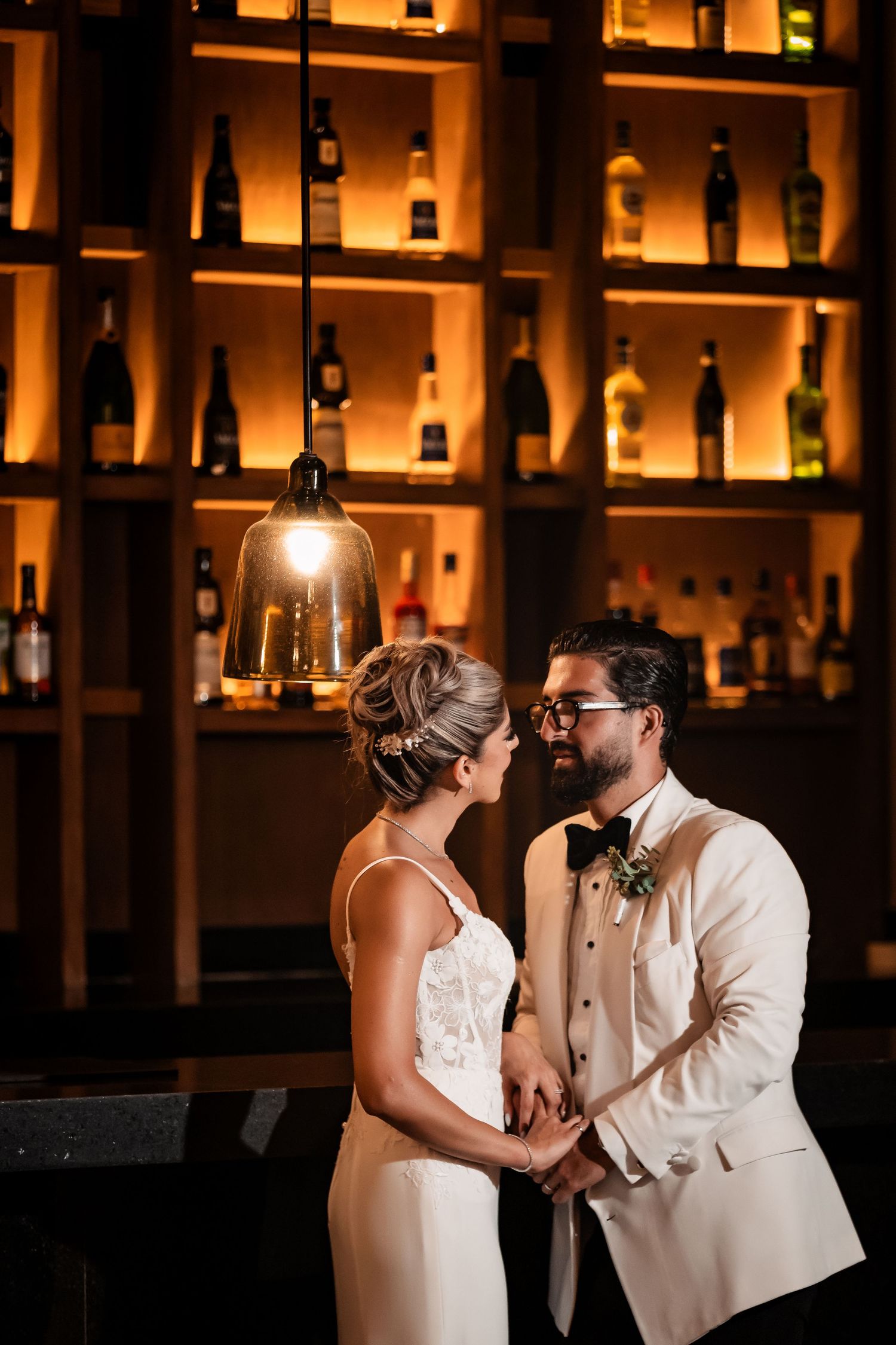 Couple sharing intimate moment in front of illuminated bar shelving with amber lighting.