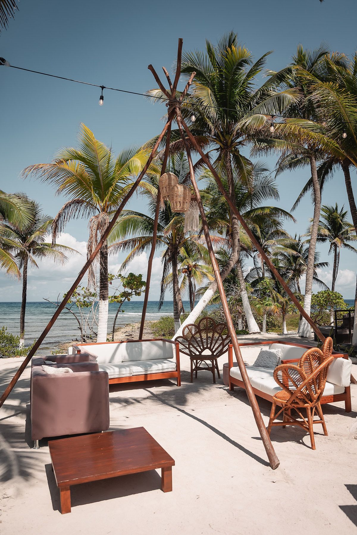Beachfront lounge area with wooden furniture and palm trees overlooking tropical ocean.