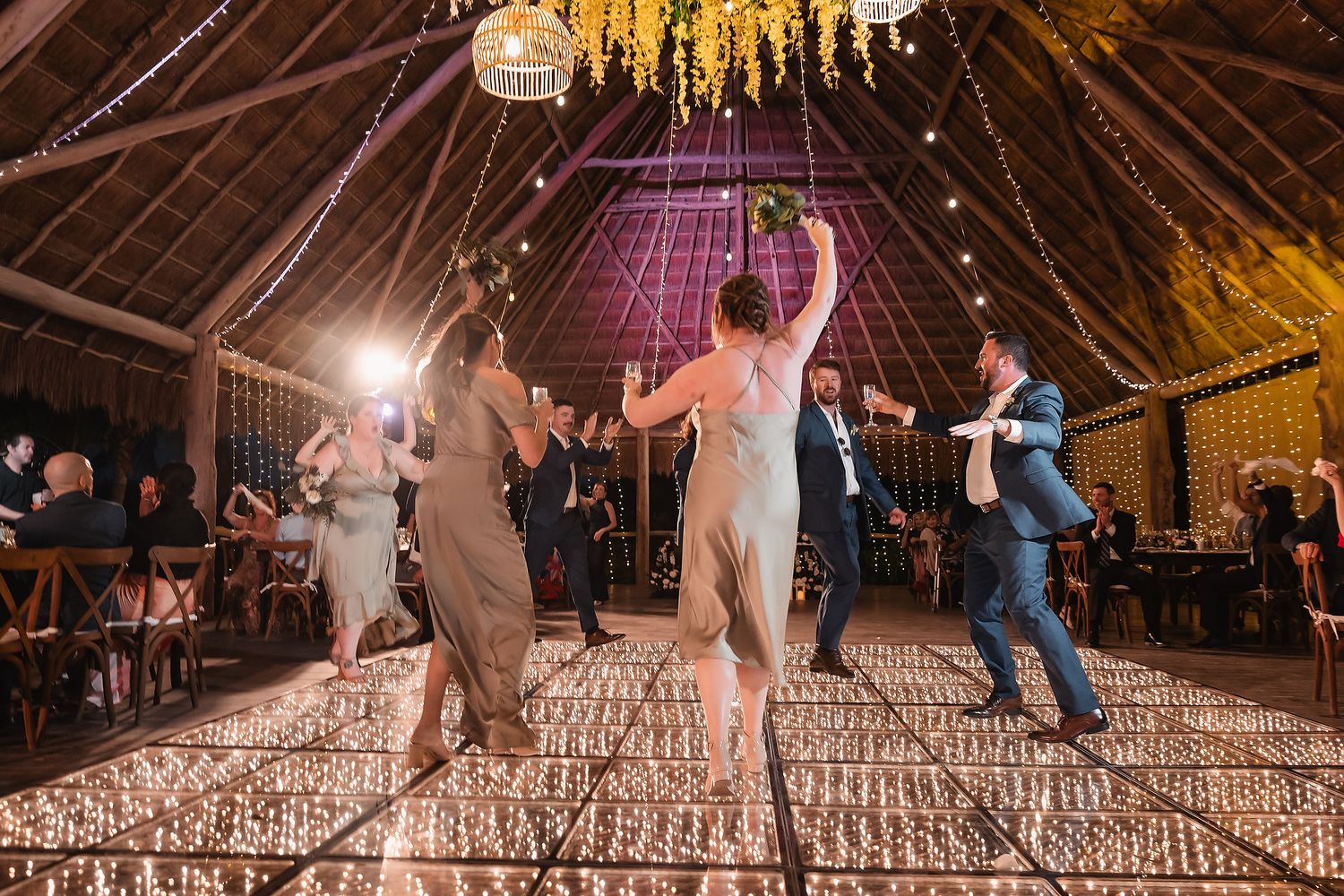 Wedding reception dance floor in a barn with dramatic lighting and yellow floral chandeliers.