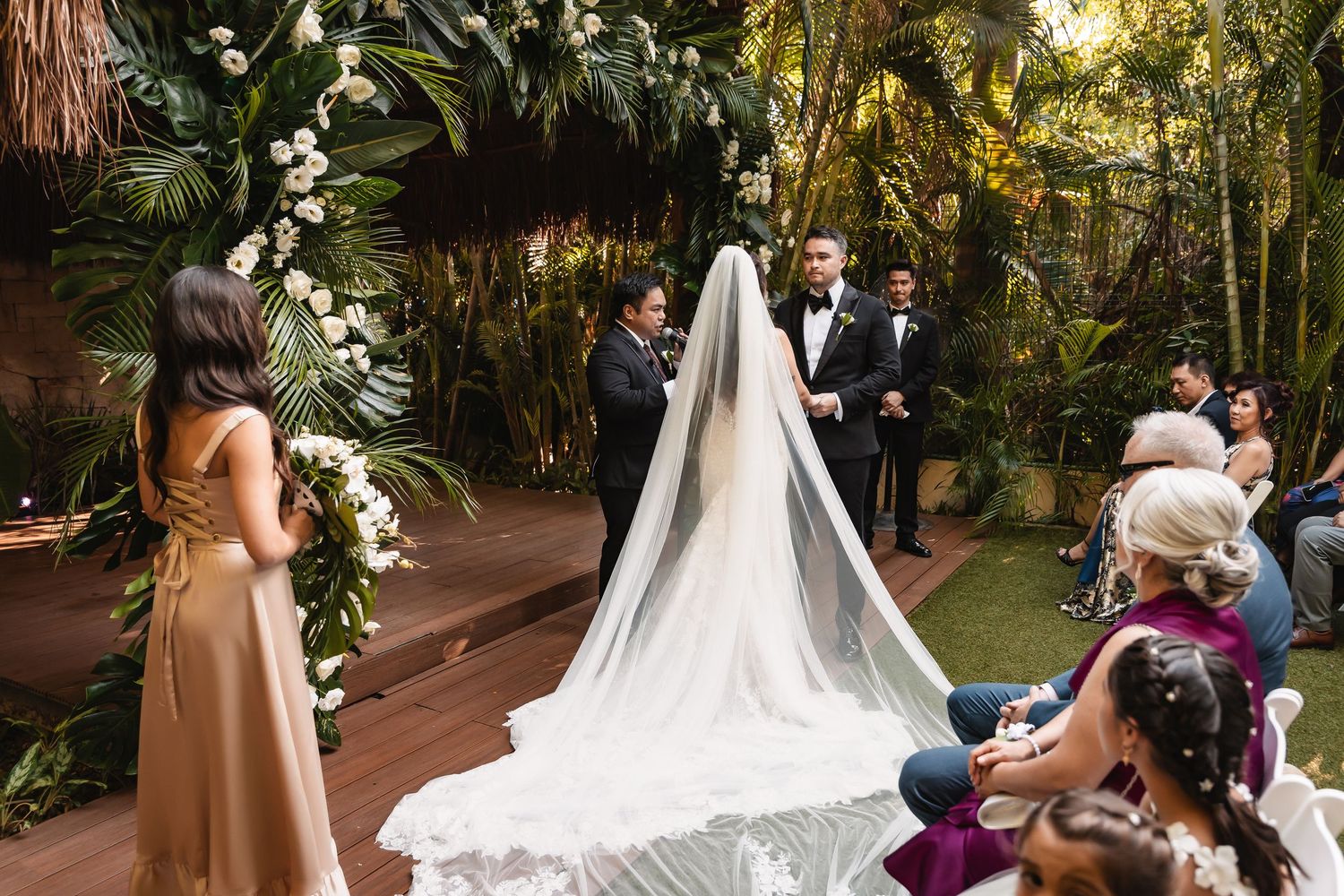 Wedding ceremony in progress at a tropical garden venue with palm trees and white flowers.