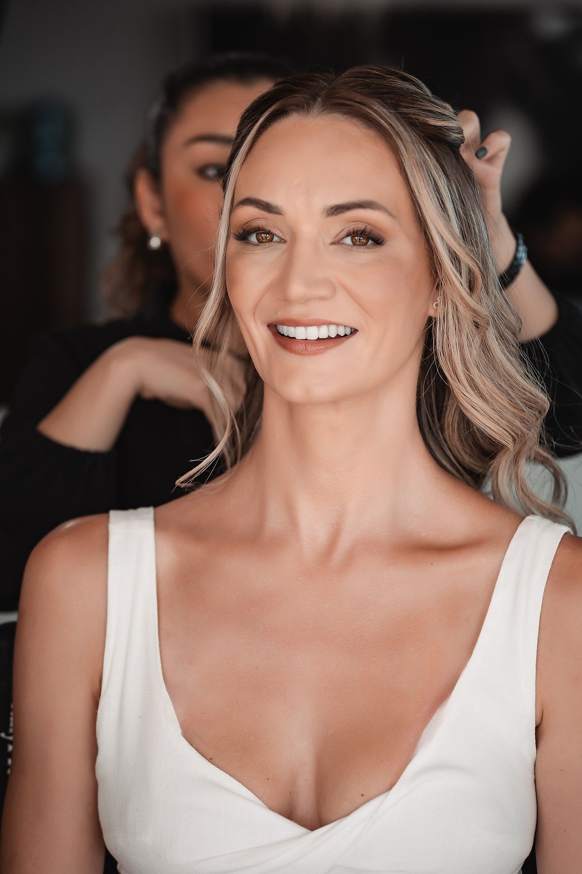 Woman in white dress smiling during wedding preparations in natural lighting.