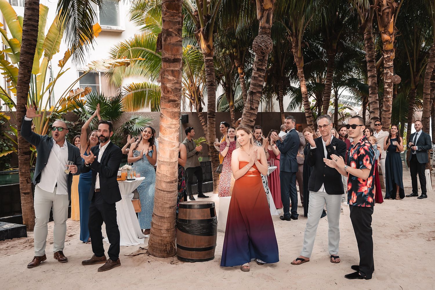 A wedding ceremony takes place under swaying palm trees on a tropical beach at sunset.