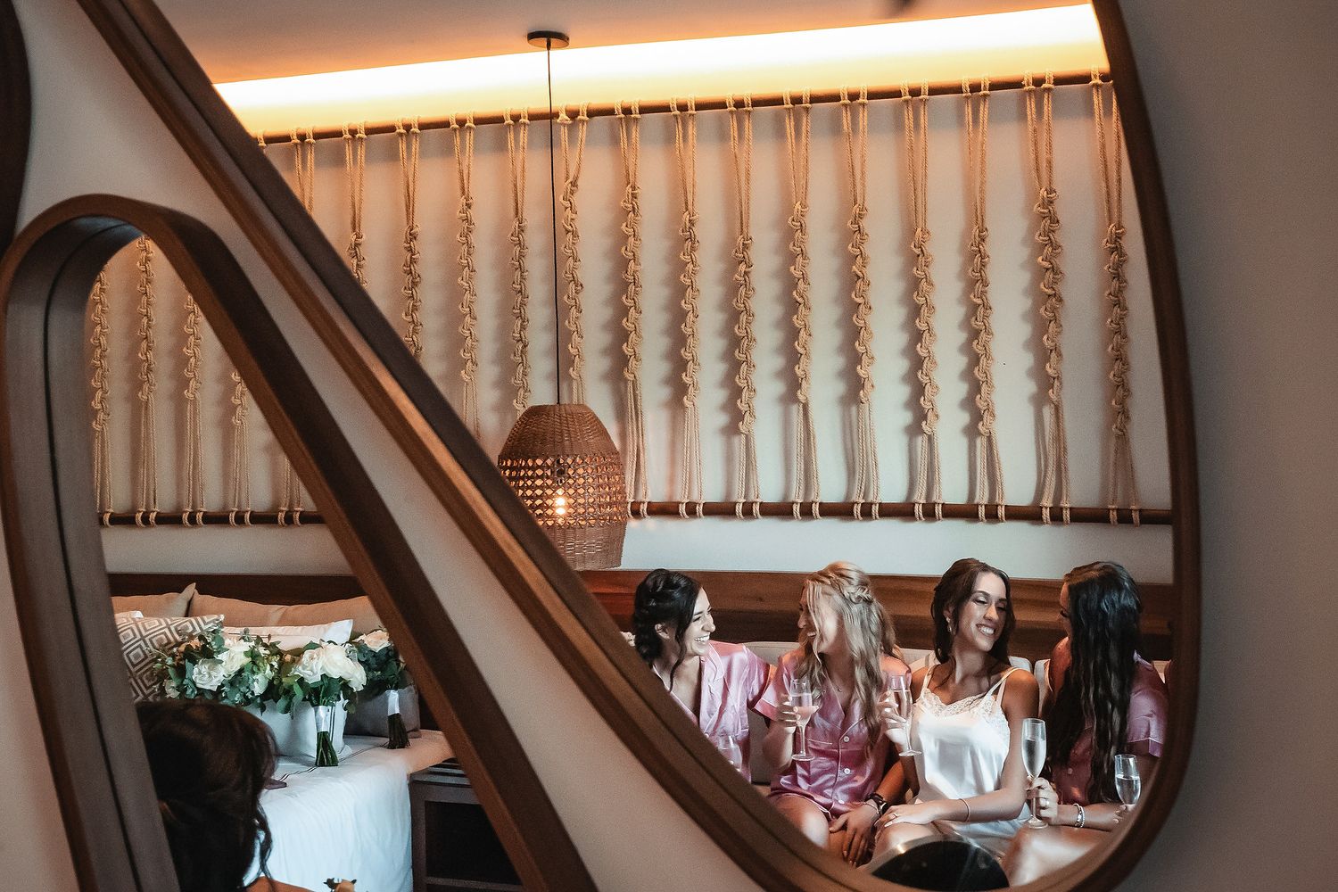 Women in silk robes socializing in a stylish boho restaurant booth with macrame wall decor and warm pendant lighting.